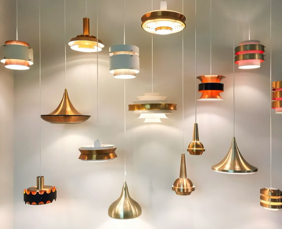 Mehrere hängende Lampen in verschiedenen Formen und Farben vor einer weißen Wand.